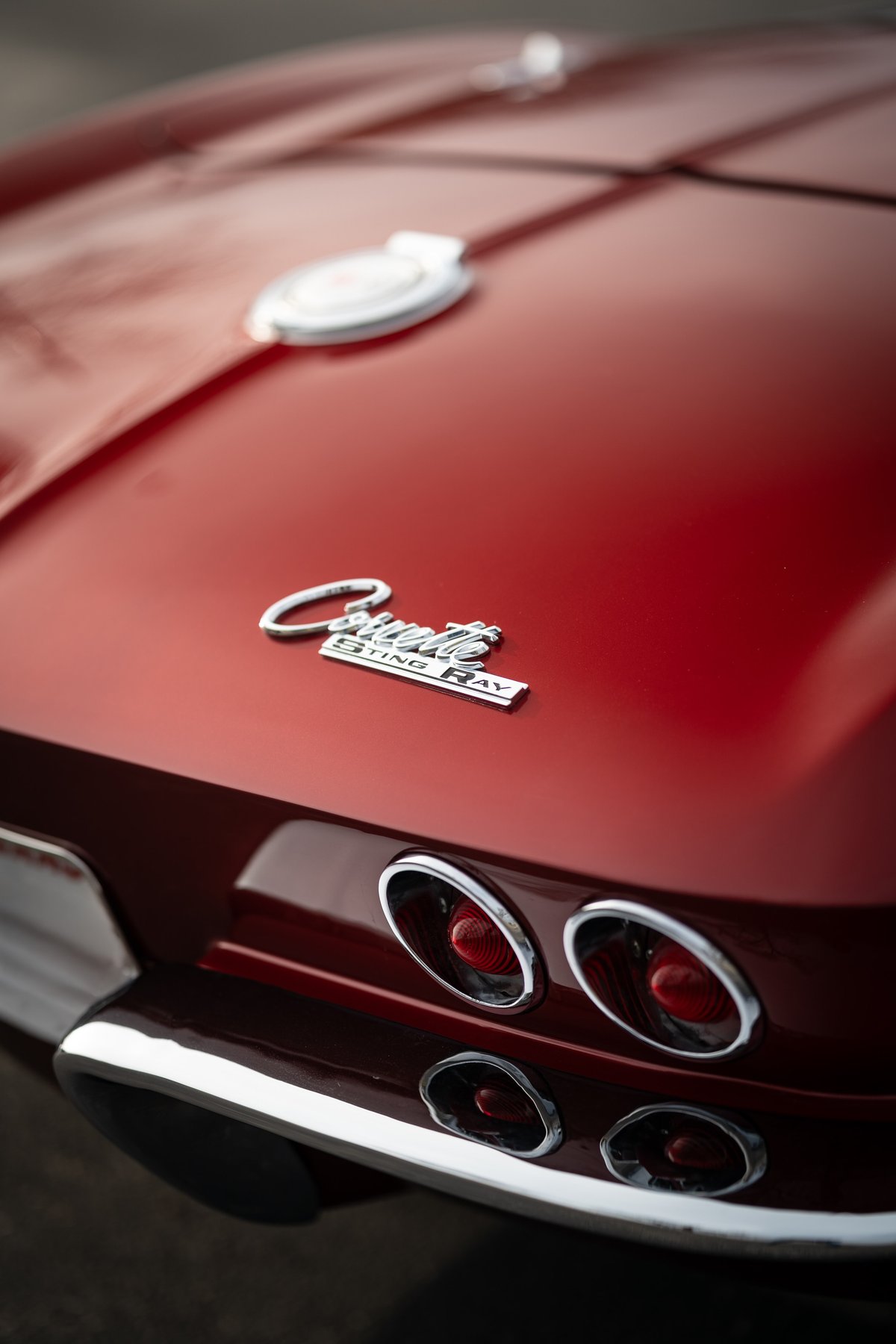 Close-up of a red 1965 Corvette Sting Ray emblem and round taillights with chrome trim.