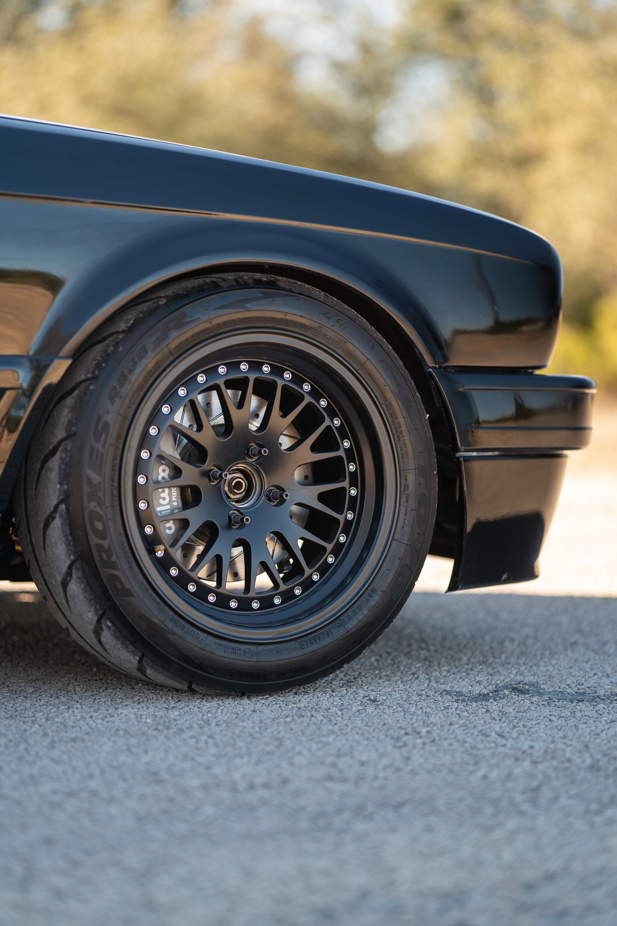 Black 1989 BMW 325is with aftermarket black multi-spoke rims and performance tires.