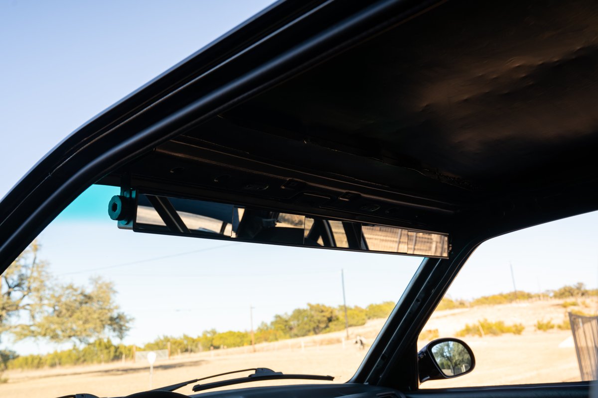 Black 1989 BMW 325is interior with aftermarket wide-angle rearview mirror.