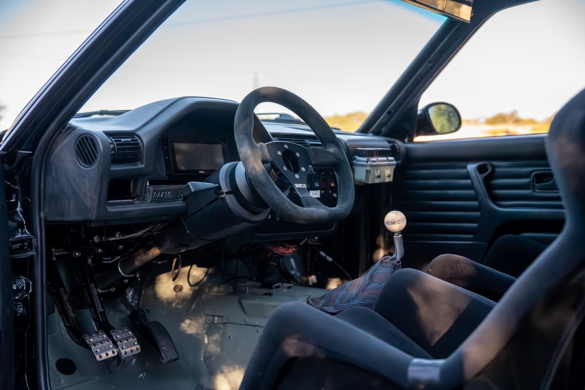 Black 1989 BMW 325is interior. Features racing seats, roll cage, and aftermarket steering wheel.