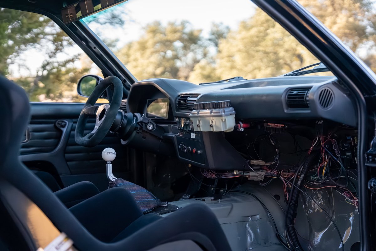 Interior view of a black 1989 BMW 325is with custom racing seats, shifter, and dashboard electronics.