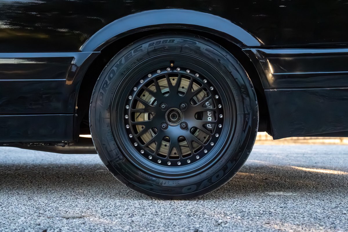 Black 1989 BMW 325is with black multi-spoke rims and performance brake calipers.