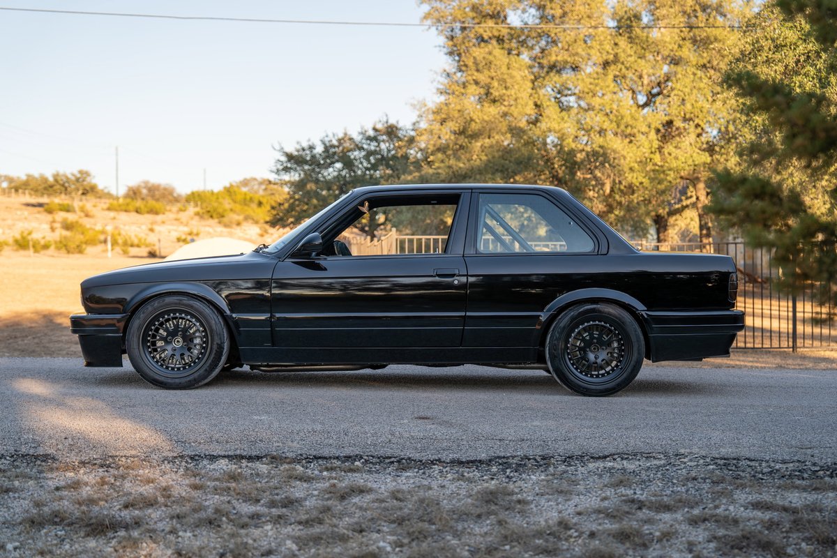 Black 1989 BMW 325is with roll cage, custom body kit, and black mesh rims.