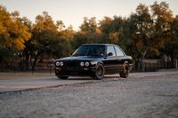 Black 1989 BMW 325is coupe with black rims, tow hook, and aftermarket trim.