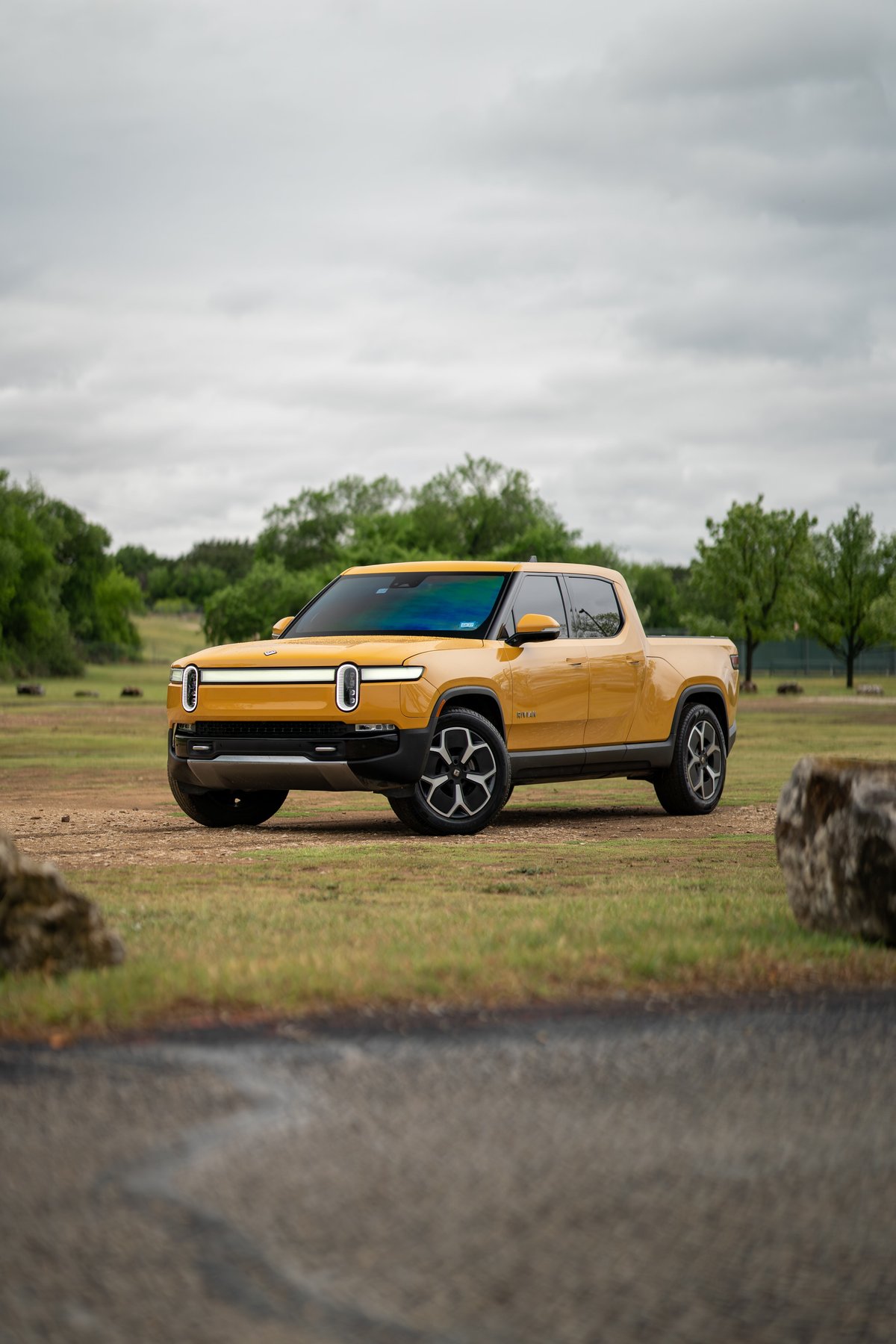 Yellow Rivian R1T pickup truck with black rims and trim parked in a grassy field.