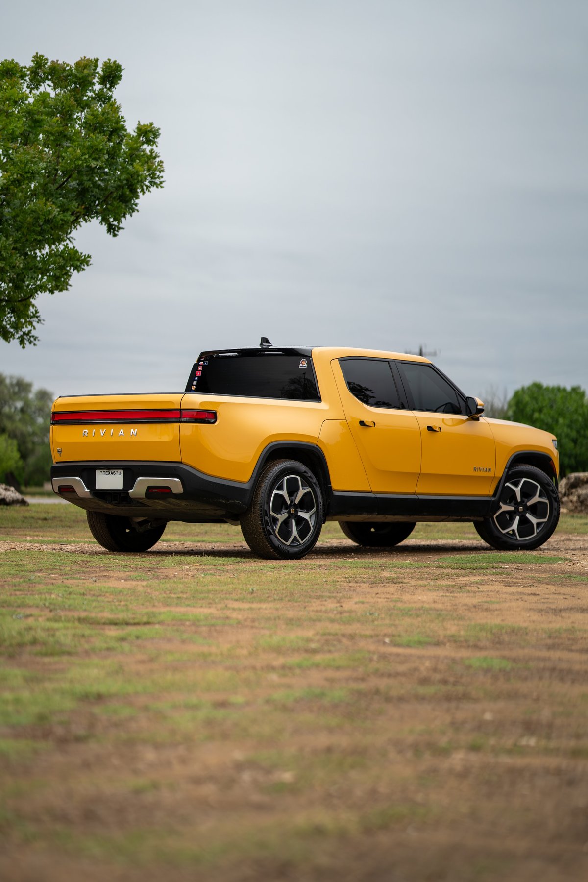 Yellow Rivian R1T electric pickup truck with black trim and machined wheels shown from the rear quarter angle.