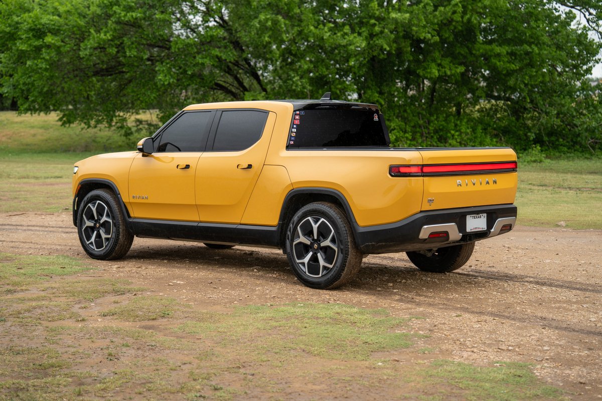 Yellow Rivian R1T electric truck with black trim and multi-spoke rims parked outdoors.