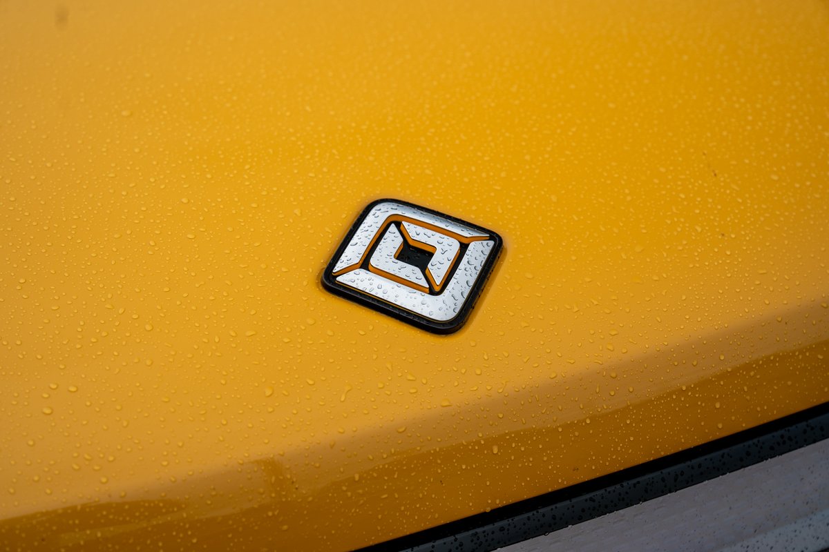 Yellow Rivian R1T badge on a wet hood, chrome and black trim accents.