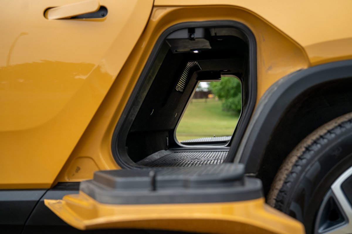 Yellow Rivian R1T shows open side storage compartment and fender trim.