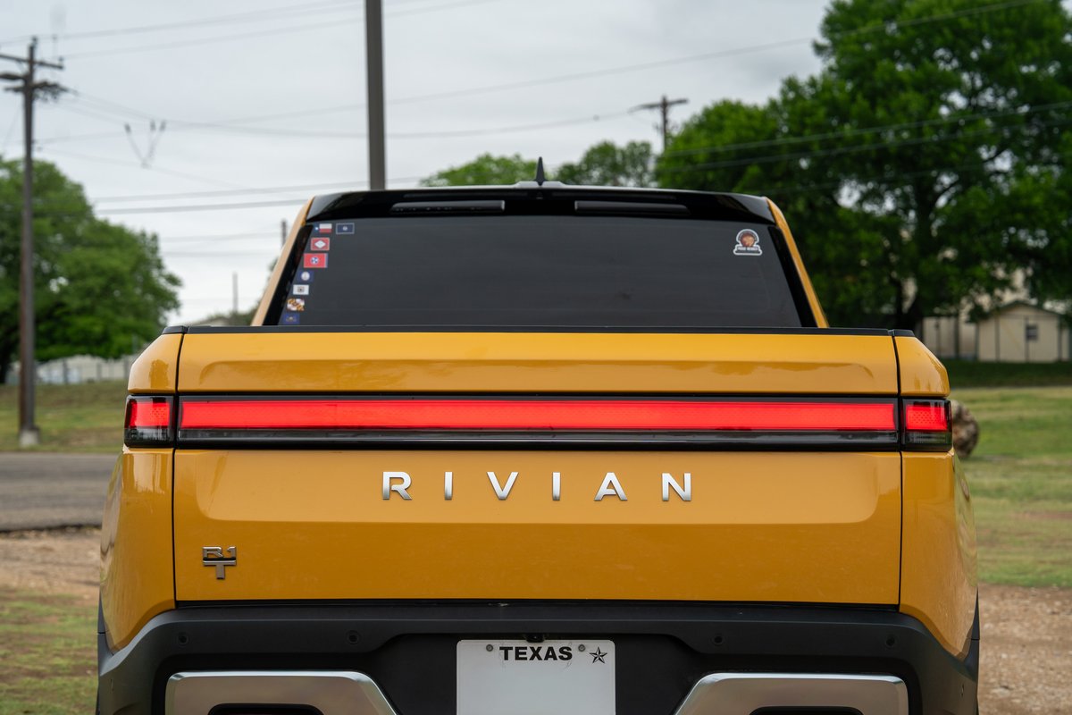 Yellow Rivian R1T rear view with full-width taillight and chrome "RIVIAN" badging.