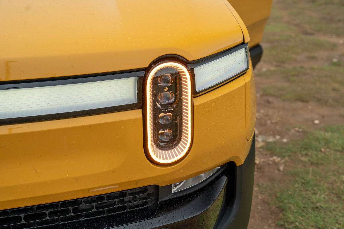 Close-up of a yellow Rivian R1T's distinctive vertical headlight with illuminated LED trim and horizontal DRL.