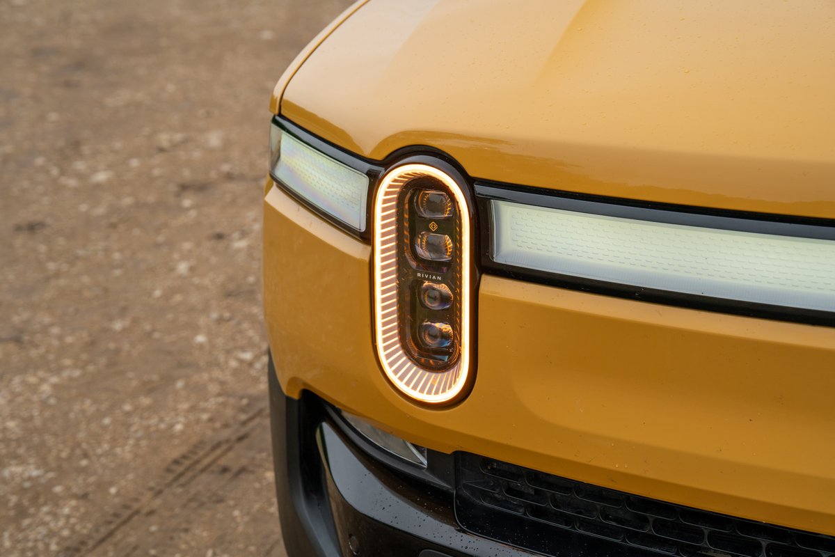 Close-up of a yellow 2022 Rivian R1T's distinctive oval headlight with LED trim.
