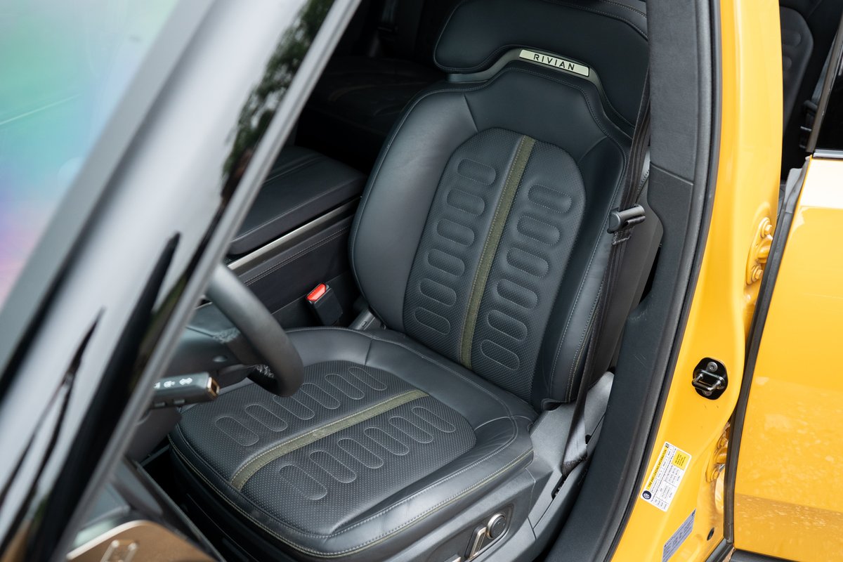 Yellow 2022 Rivian R1T driver's seat with perforated leather, green trim, and Rivian logo.