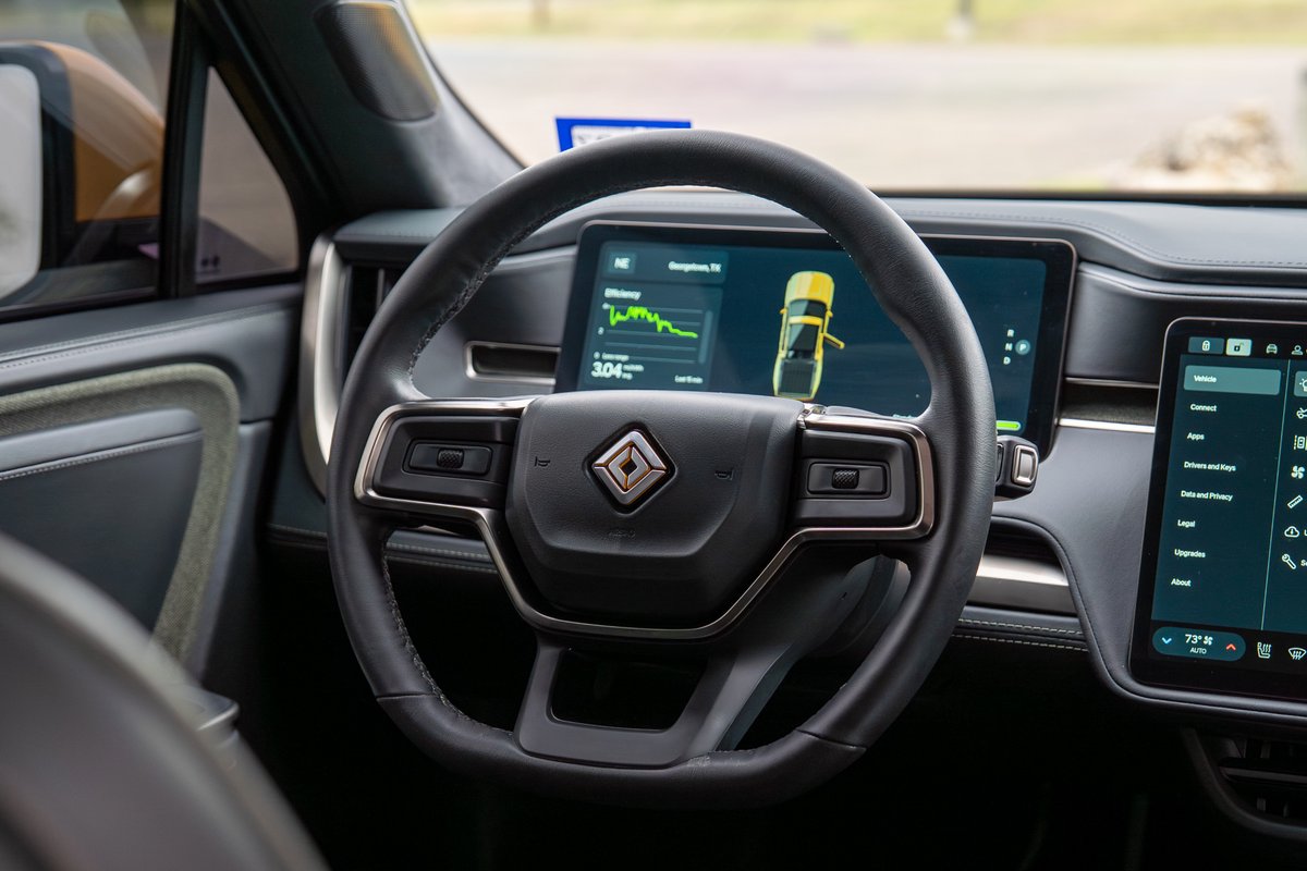Interior of a yellow Rivian R1T, showing the steering wheel, dashboard, and infotainment screens.