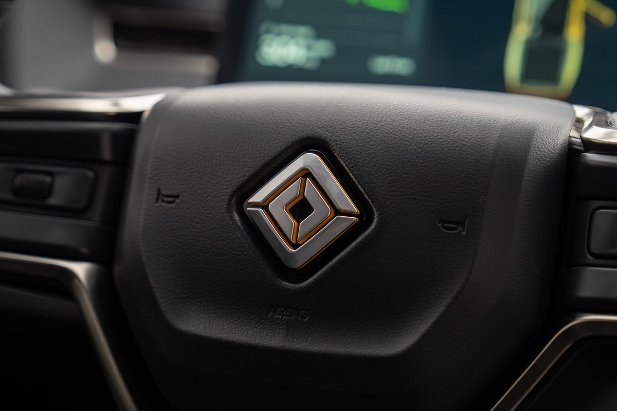 Close-up of the steering wheel in a yellow 2022 Rivian R1T, featuring the illuminated logo.