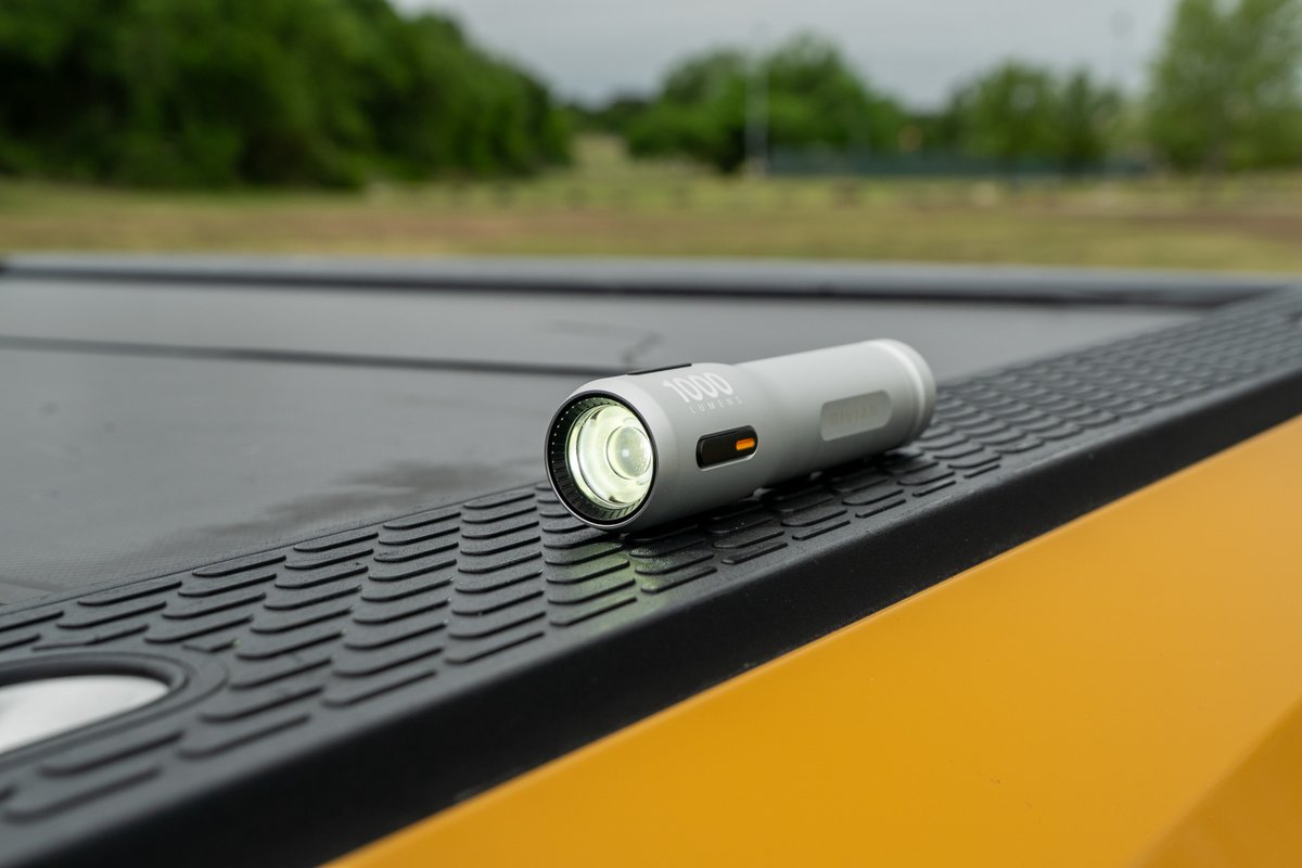 Silver Rivian R1T flashlight resting on textured black trim and yellow exterior.