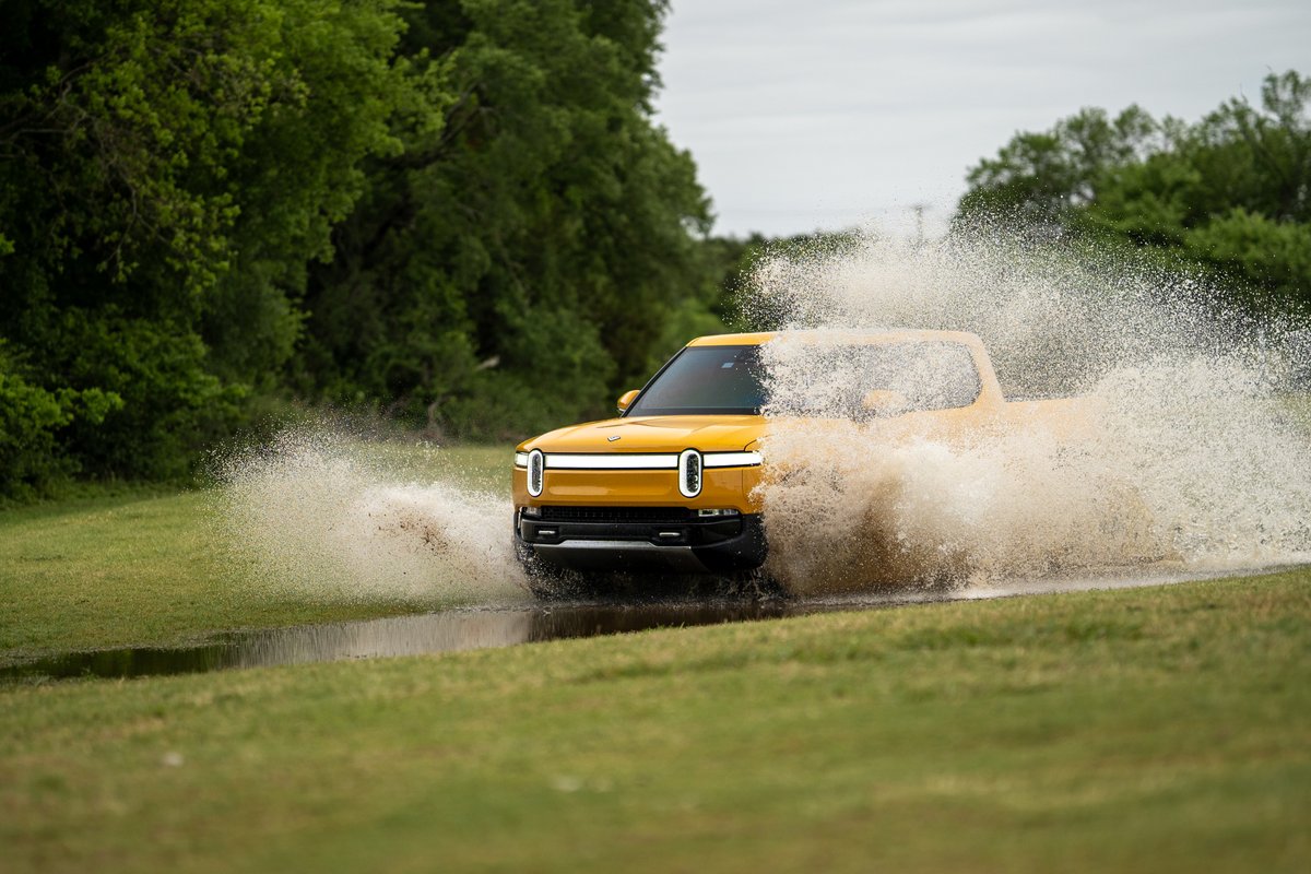 Yellow Rivian R1T pickup truck splashing through water.