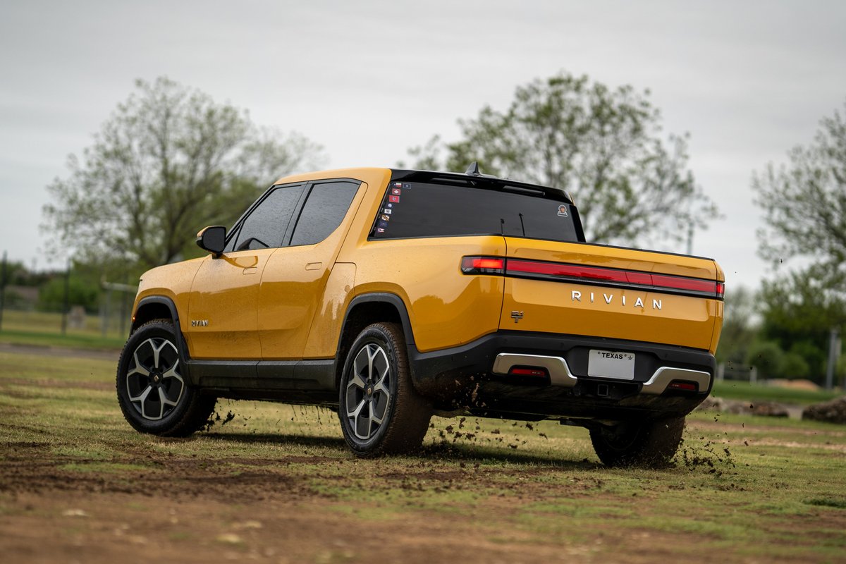 Yellow 2022 Rivian R1T with black accents and multi-spoke rims driving off-road.