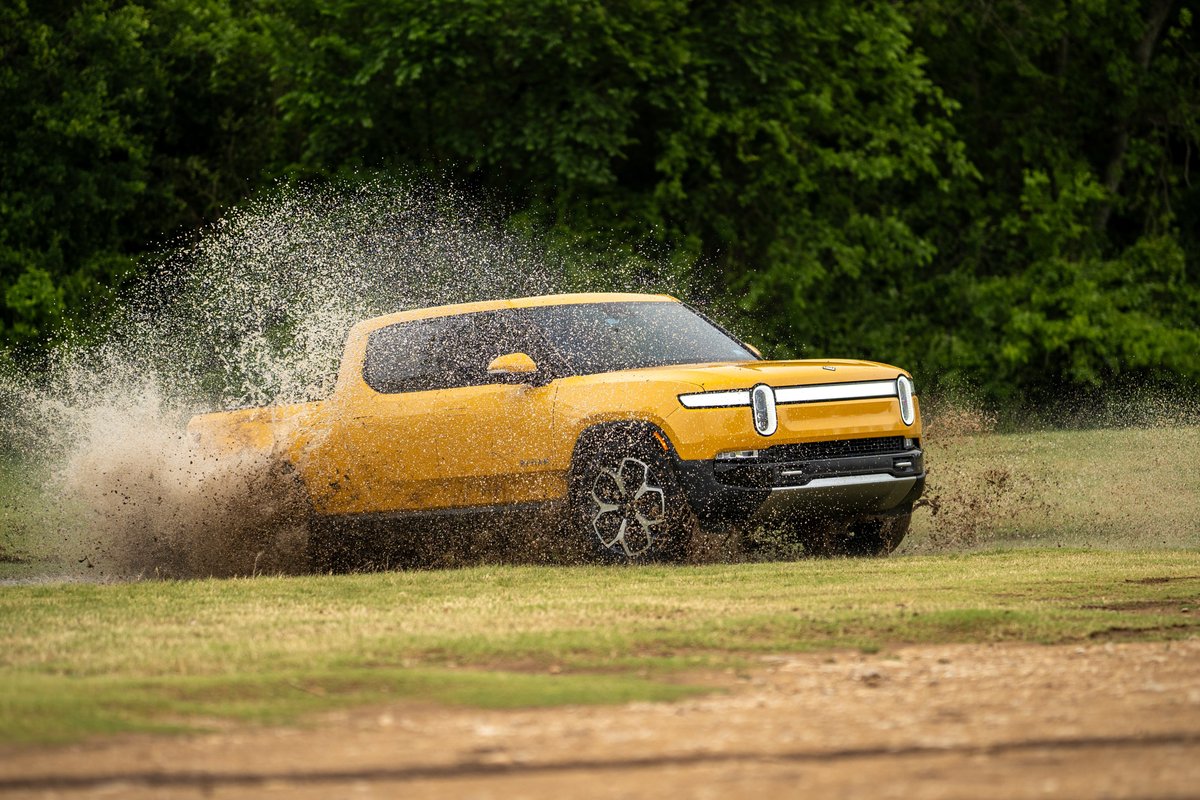 Yellow Rivian R1T electric truck kicking up mud and water on off-road terrain.