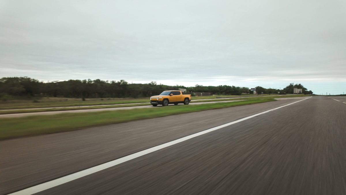 Yellow Rivian R1T driving on a highway with a blur effect.