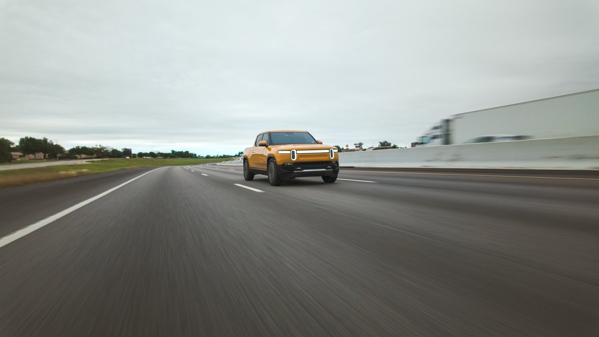 Yellow Rivian R1T electric pickup truck driving on highway with motion blur.