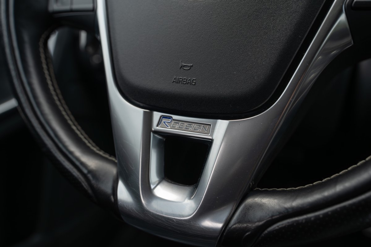 Close-up of a 2015 Volvo V60 R-Design steering wheel with brushed metal trim and R-Design badging.