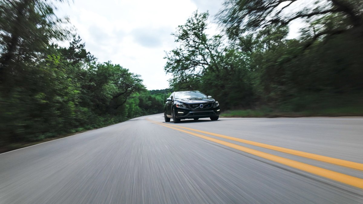Black 2015 Volvo V60 R-Design Polestar drives on a tree-lined road.