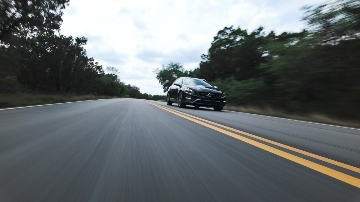 Black 2015 Volvo V60 R-Design Polestar drives on a road with double yellow lines.