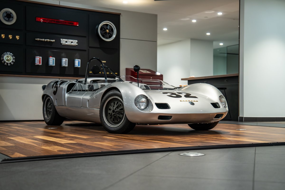 Silver 1964 Elva Porsche 4-Cam race car with black rims and racing livery.