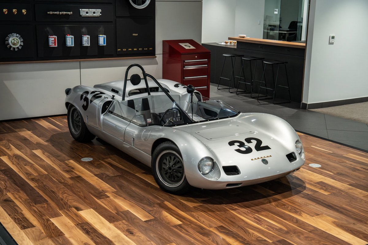 1964 Elva Porsche 4-Cam race car with silver livery and black racing numbers 32 on a wooden floor.
