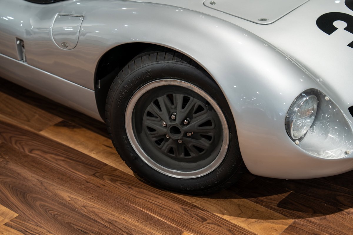 Close-up of a silver 1964 Elva Porsche 4-Cam with a black multi-spoke rim and polished lip.