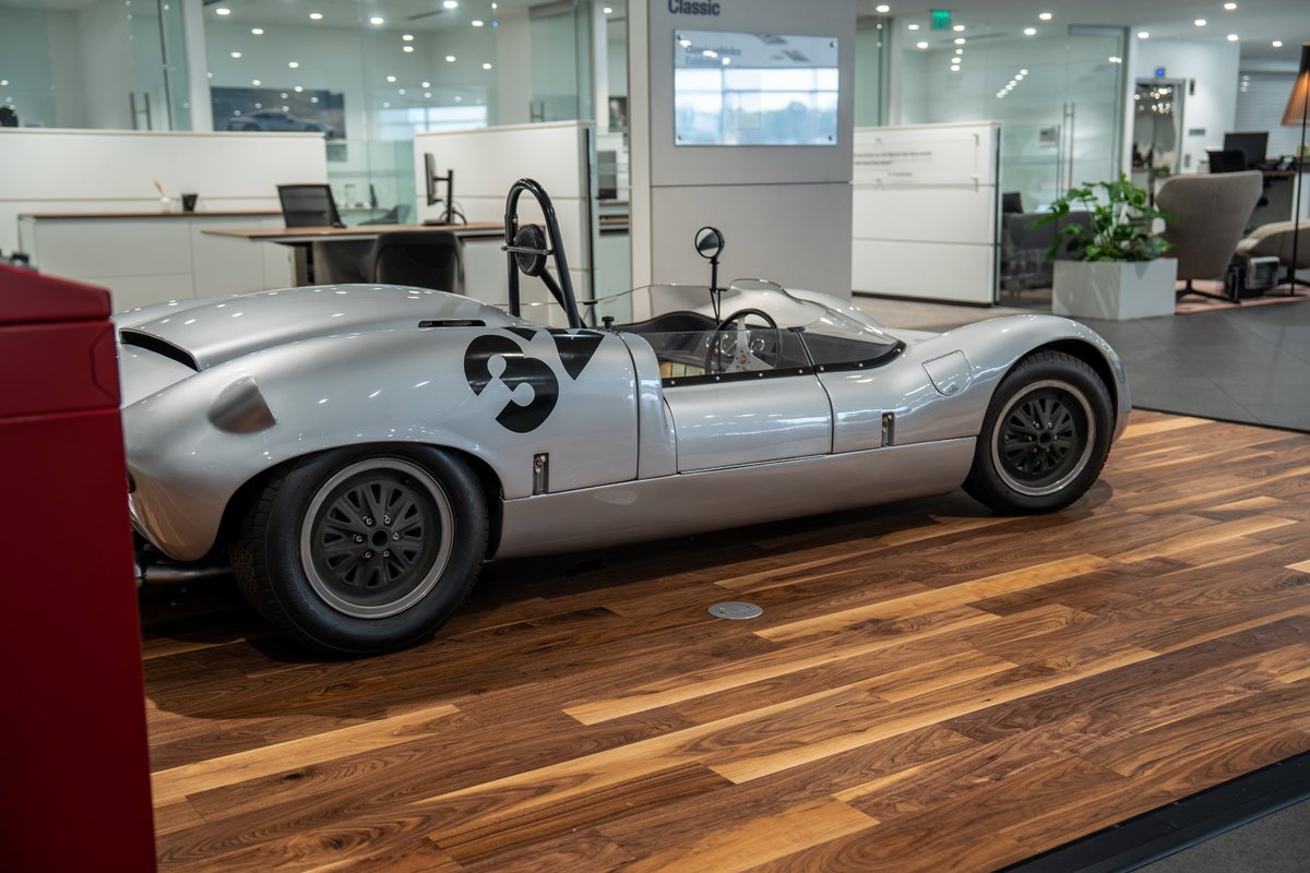 A silver 1964 Elva Porsche 4-Cam race car with black 'SV' livery and wire-spoke rims.