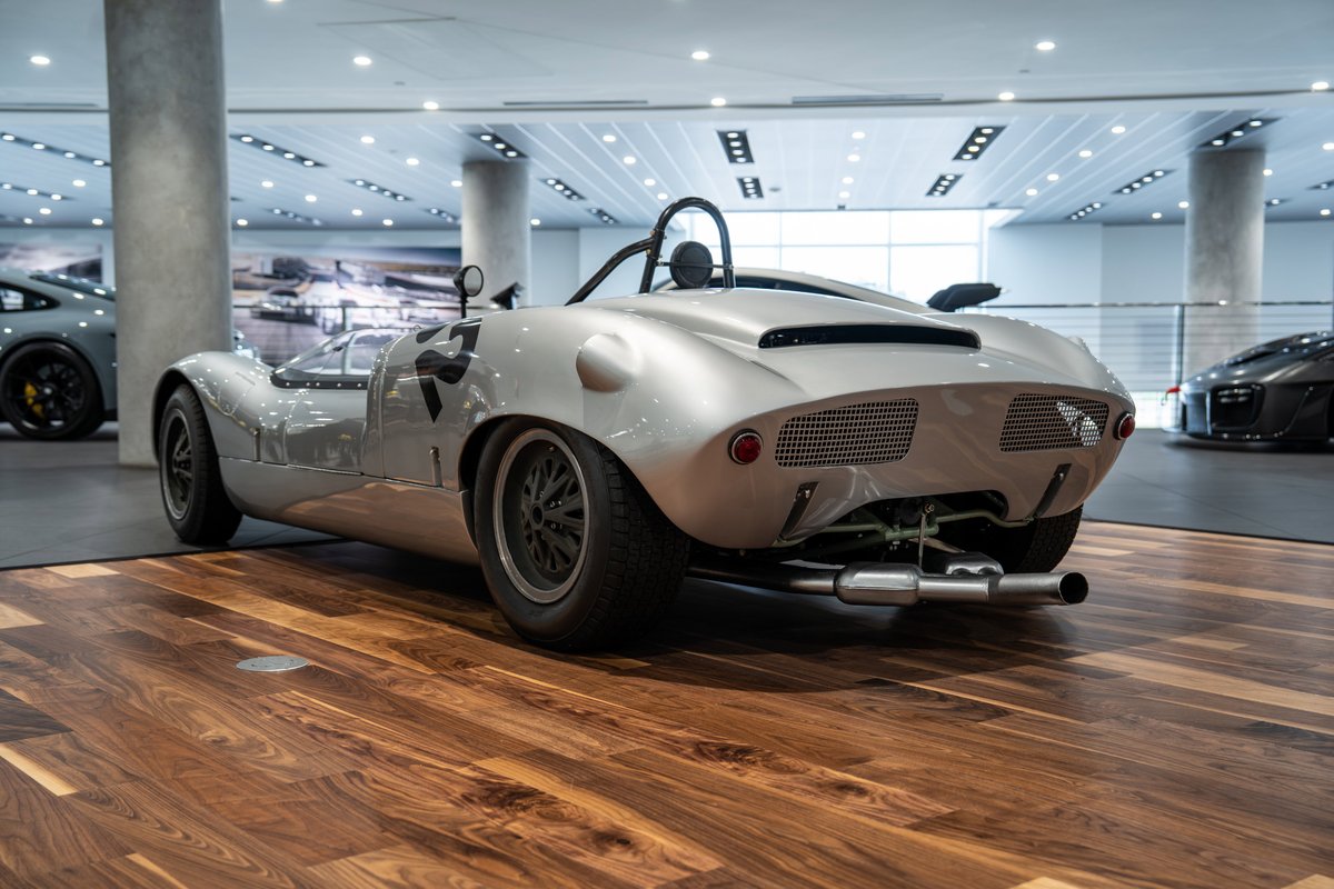 Silver 1964 Elva Porsche 4-Cam race car with black livery on rims and racing number 77.