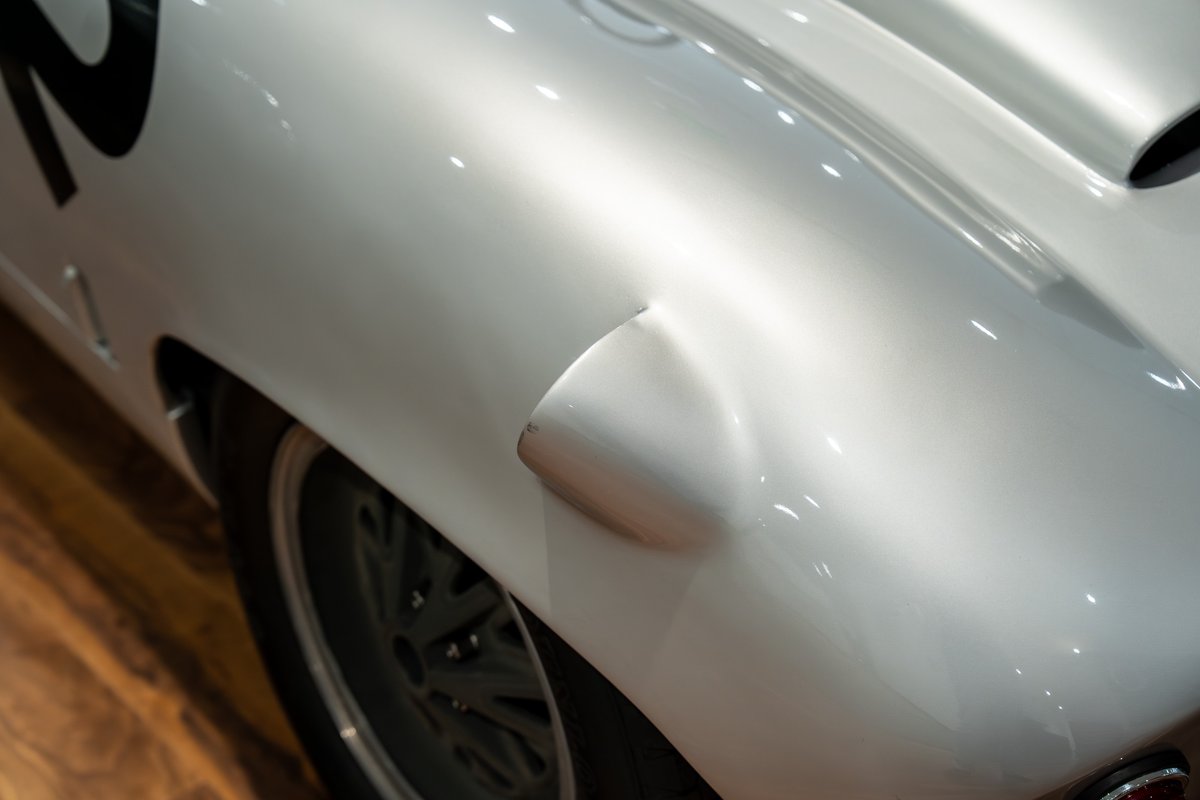Close-up of a silver 1964 Elva Porsche 4-Cam's rear fender, showing race livery.