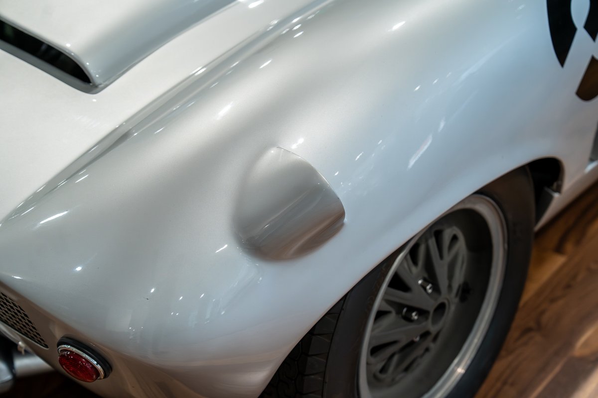Close-up of a silver 1964 Elva Porsche 4-Cam's rear fender, showing a racing stripe and alloy rims.
