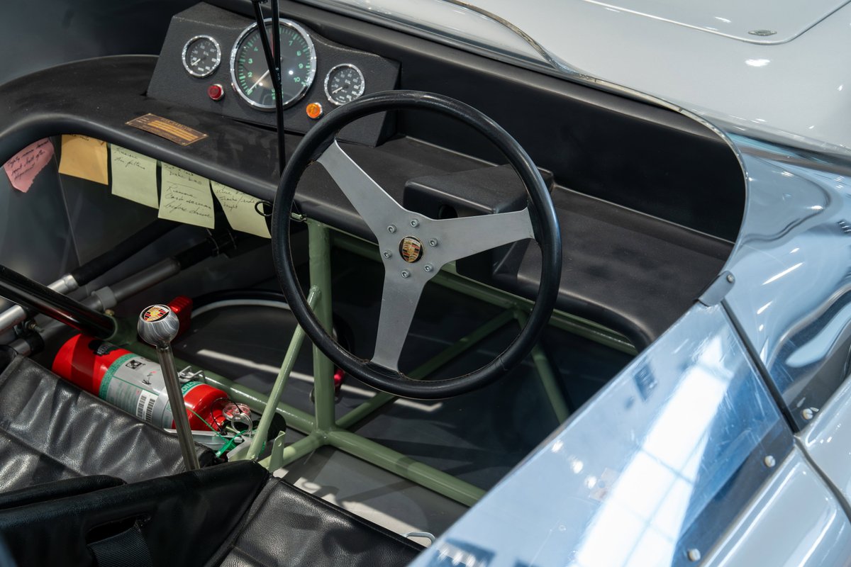 Vintage Elva Porsche 4-cam race car interior with a three-spoke steering wheel, gauges, and fire extinguisher.