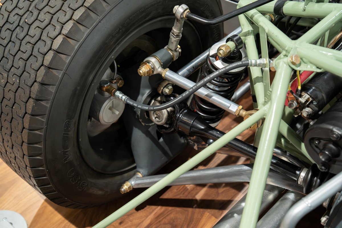Close-up of a vintage 1964 Elva Porsche 4-cam's black tire, green tubular chassis, and suspension system.