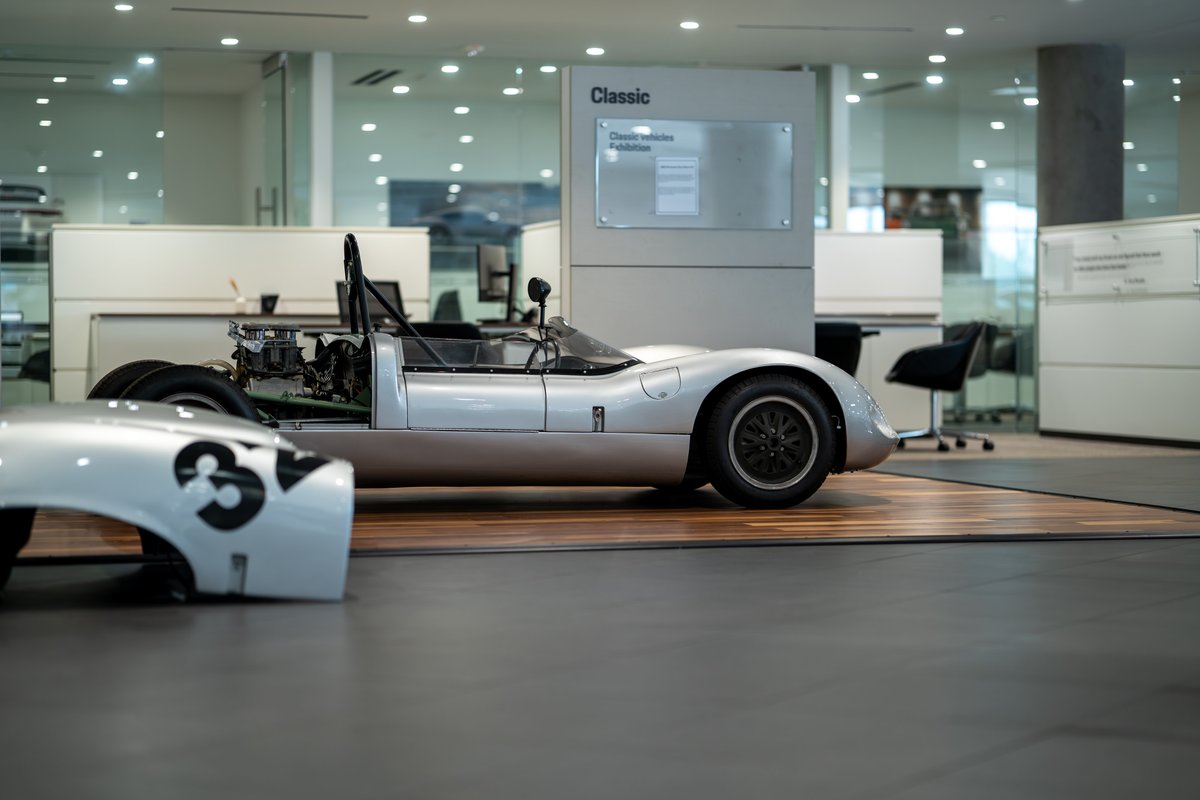 1964 Elva Porsche 4 Cam racer in silver, exposed engine, black rims, minimalist livery.