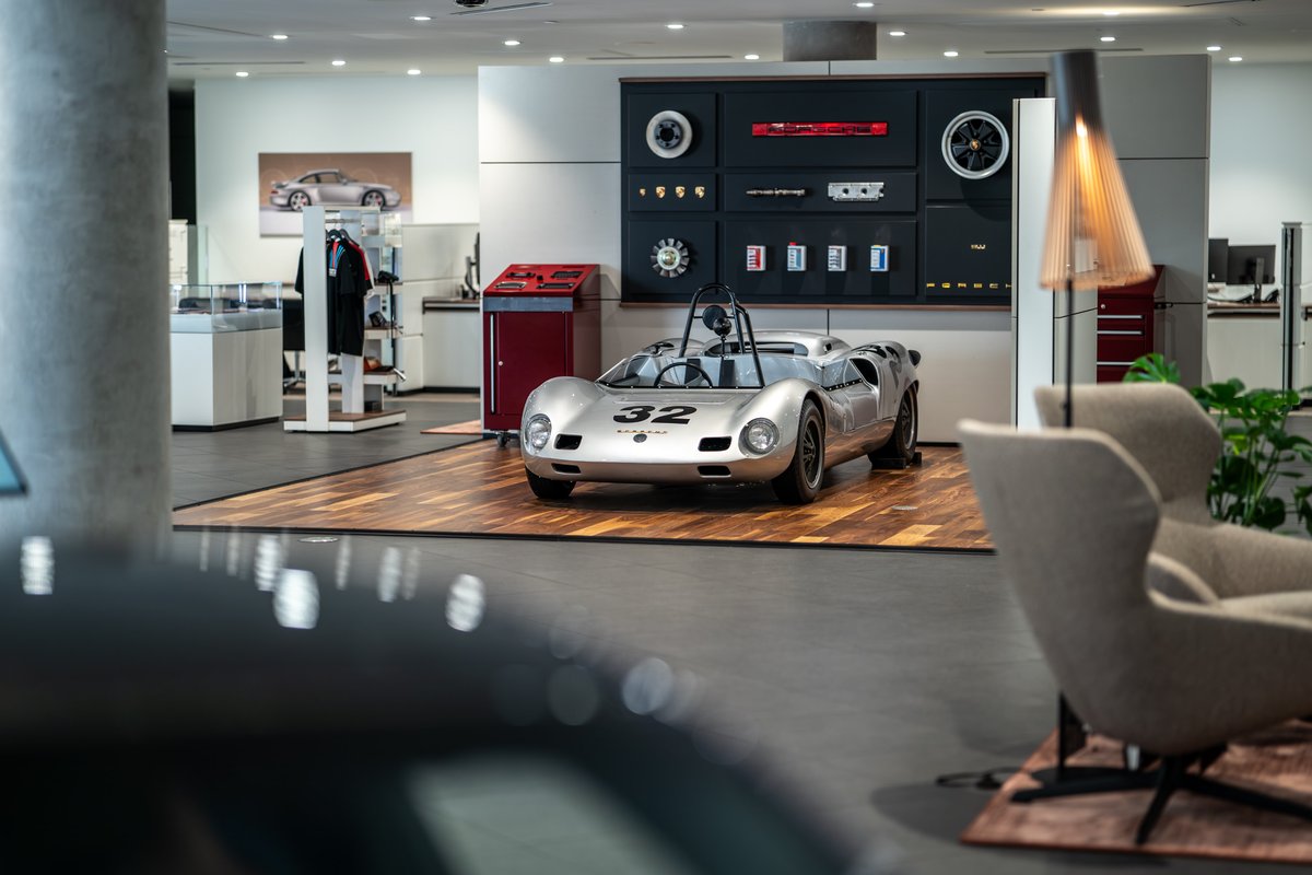 Silver 1964 Elva Porsche 4-Cam race car with number 32 livery on display in a showroom.