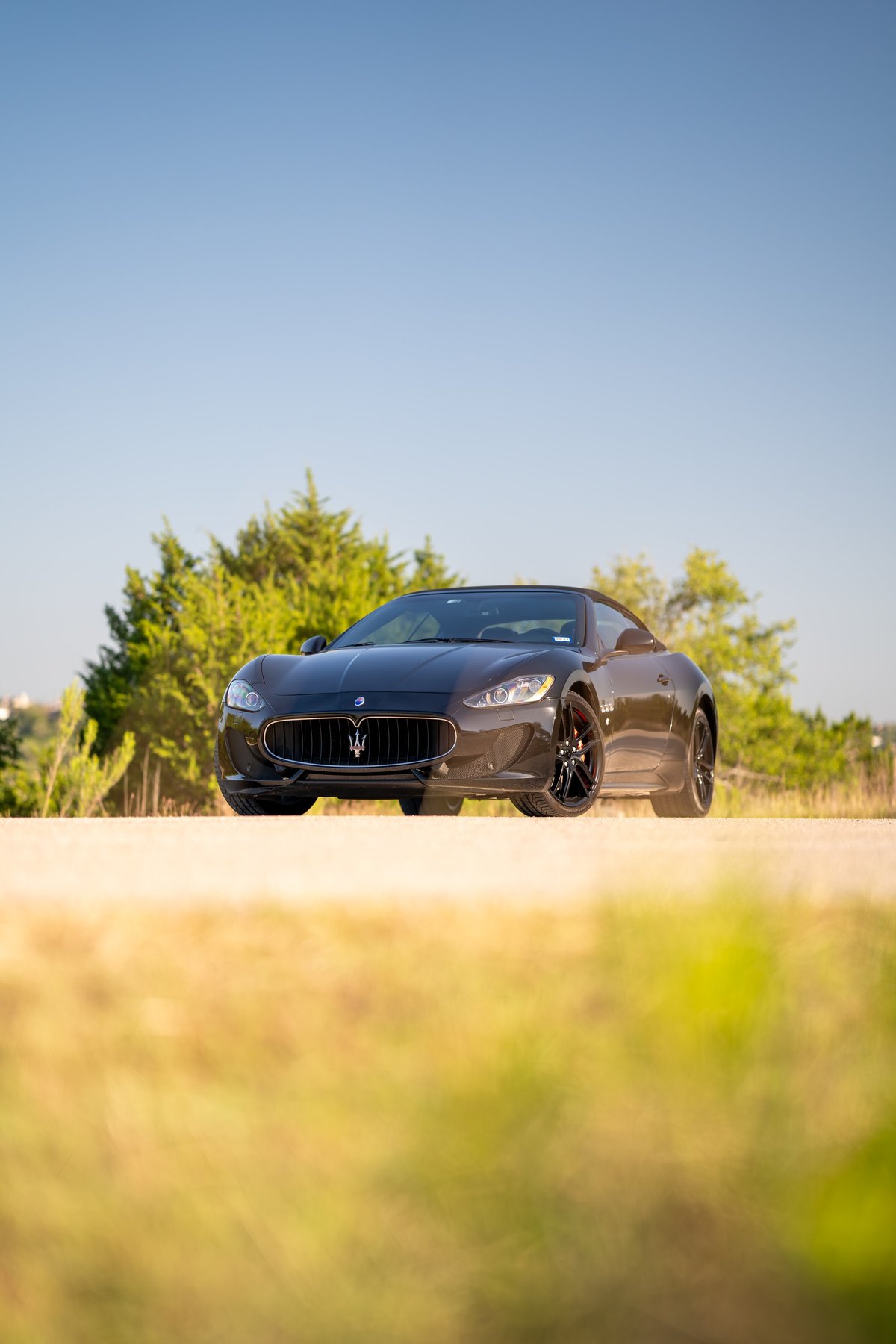 Front view of a dark gray 2016 Maserati GranTurismo convertible with black rims and red brake calipers.