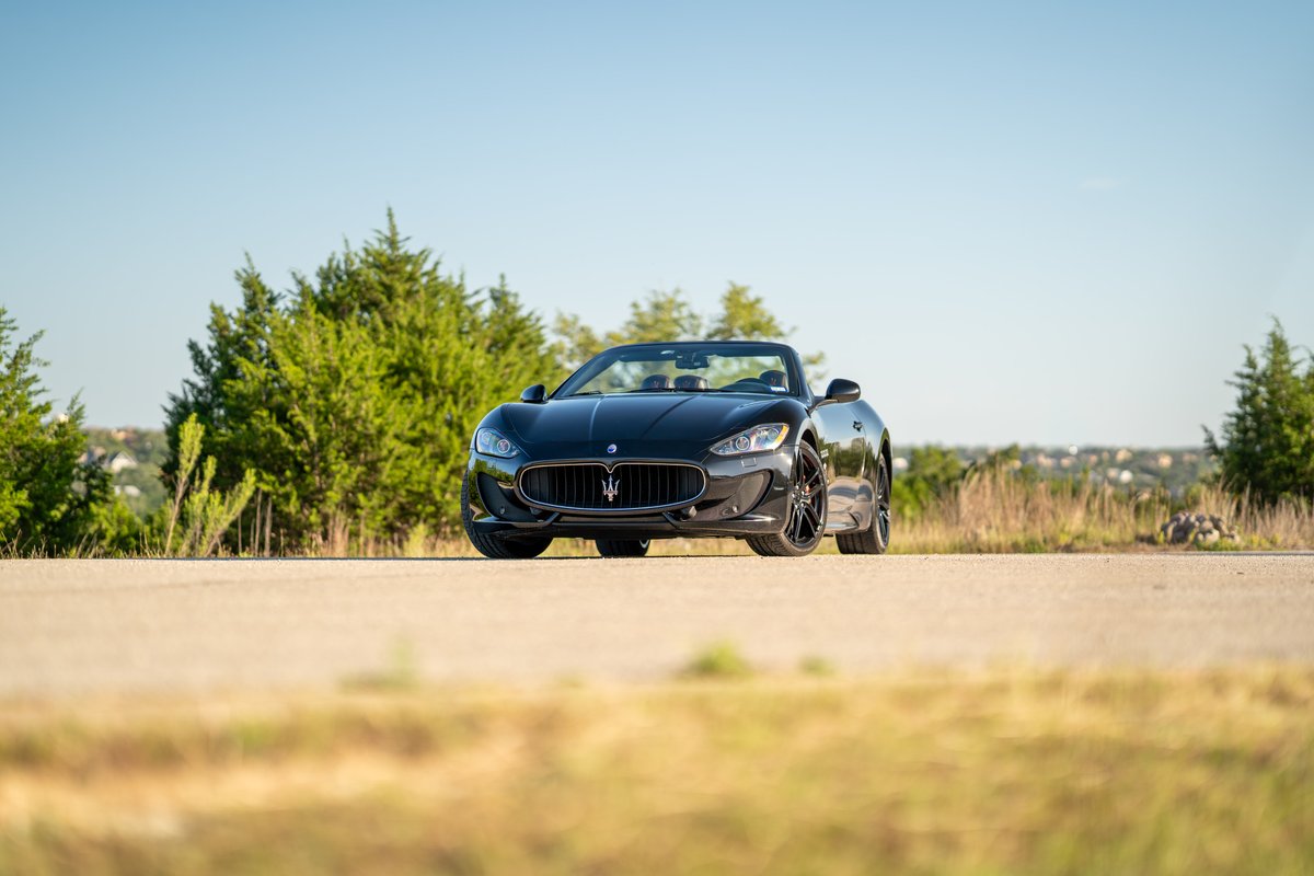 Black 2016 Maserati GranTurismo convertible with dark rims parked on a road.