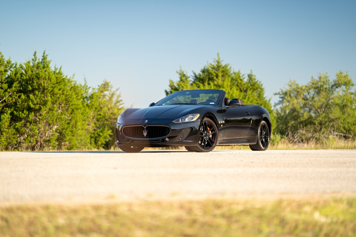 Black 2016 Maserati GranTurismo Convertible with black rims parked on a dirt road with trees.