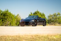 Black 2016 Maserati GranTurismo Convertible with black rims parked on a dirt road with trees.