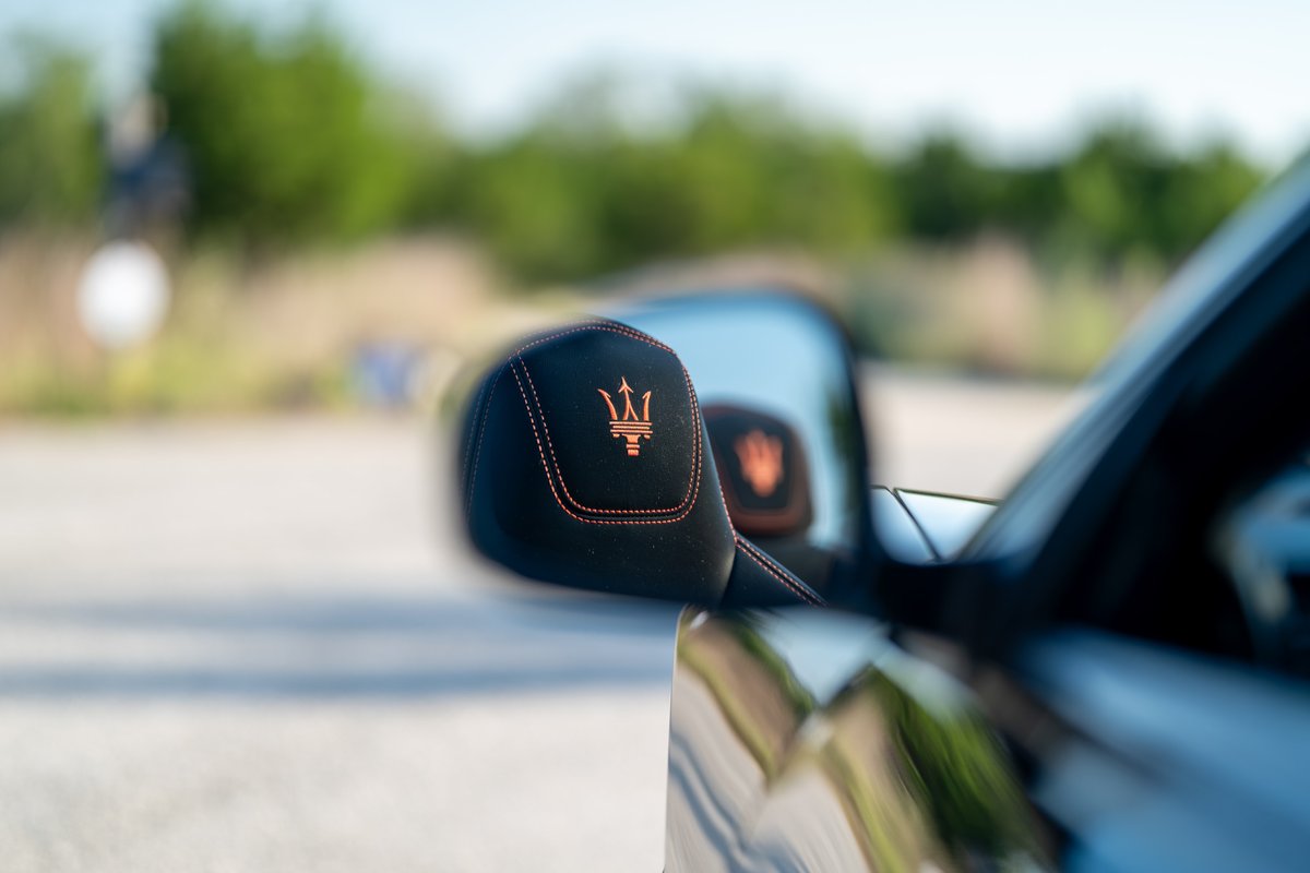 Black Maserati GranTurismo with embroidered trident logo on headrest and orange stitching.