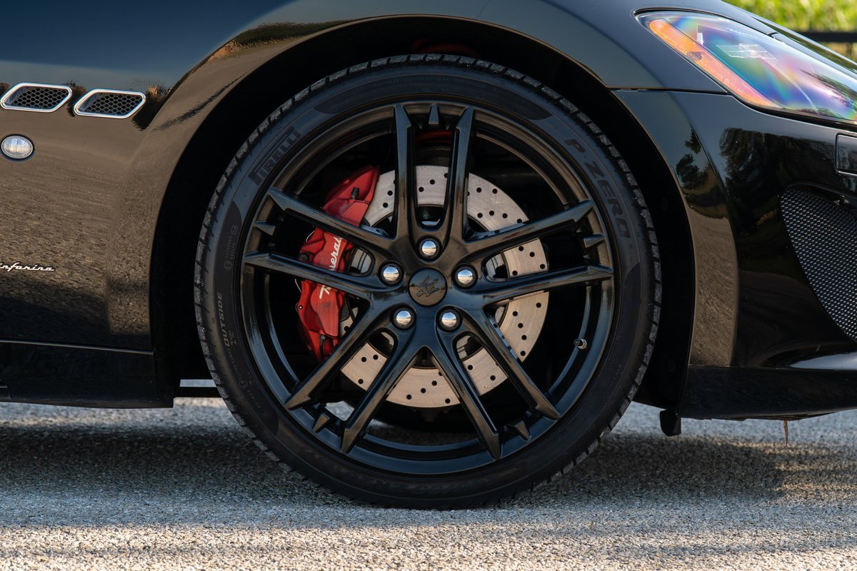 Close-up of a black Maserati GranTurismo wheel with red brake calipers and perforated rotors.