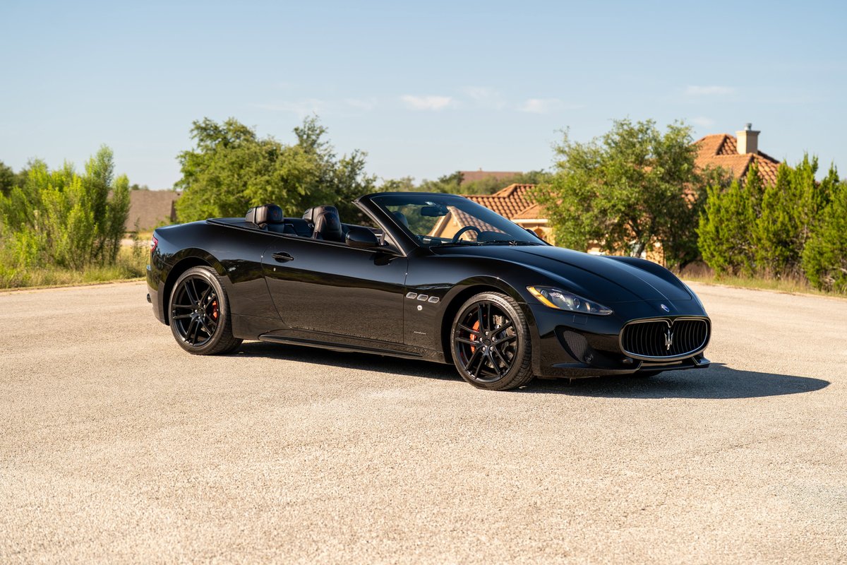 Black 2016 Maserati GranTurismo convertible with red brake calipers and black rims parked outdoors.