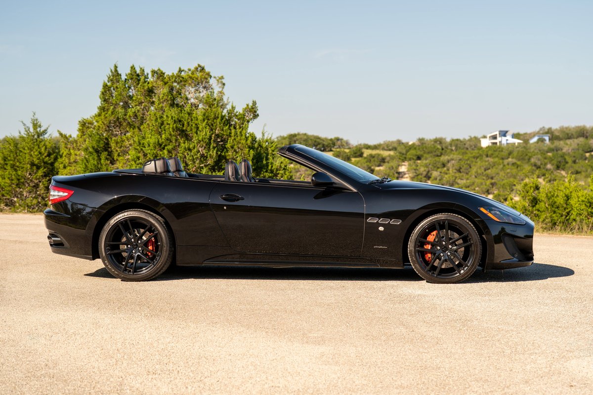Side profile of a black 2016 Maserati GranTurismo convertible with black rims and red brake calipers.