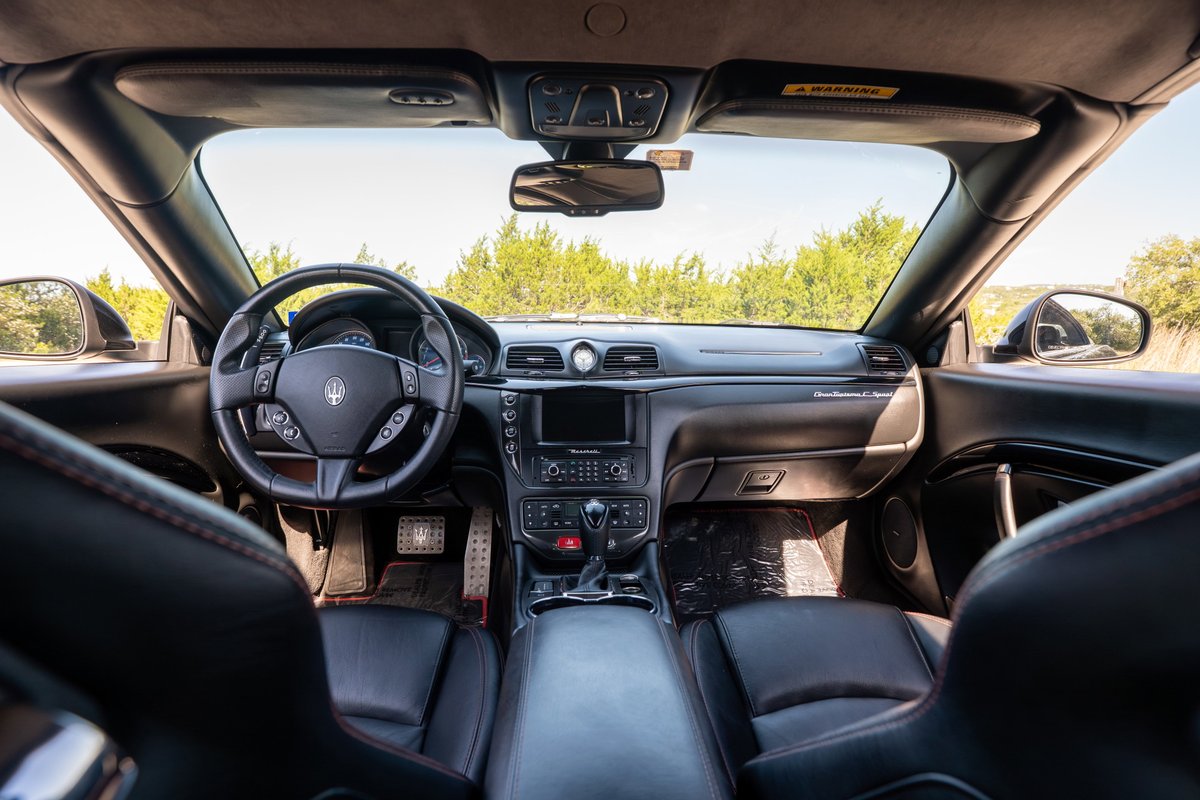 Maserati GranTurismo interior. Black leather seats, steering wheel, and dashboard trim with red stitching.