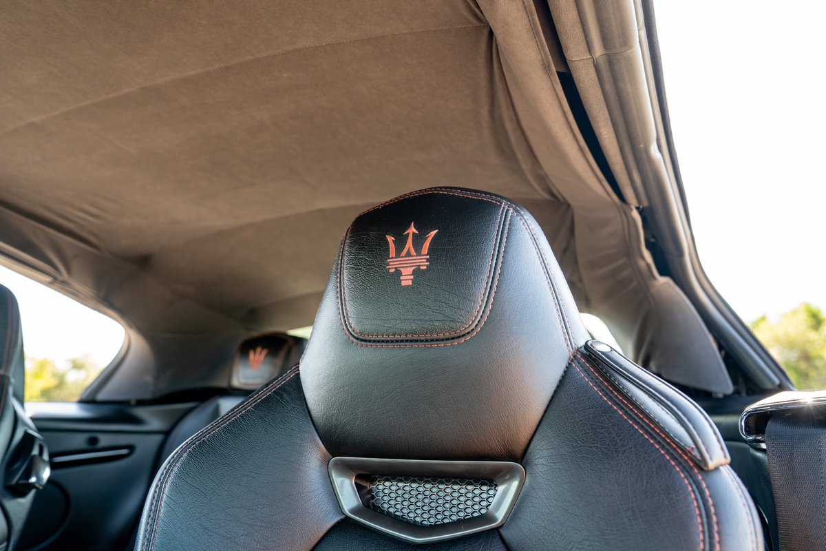 Close-up on black leather Maserati GranTurismo seats with orange stitching and trident logo.