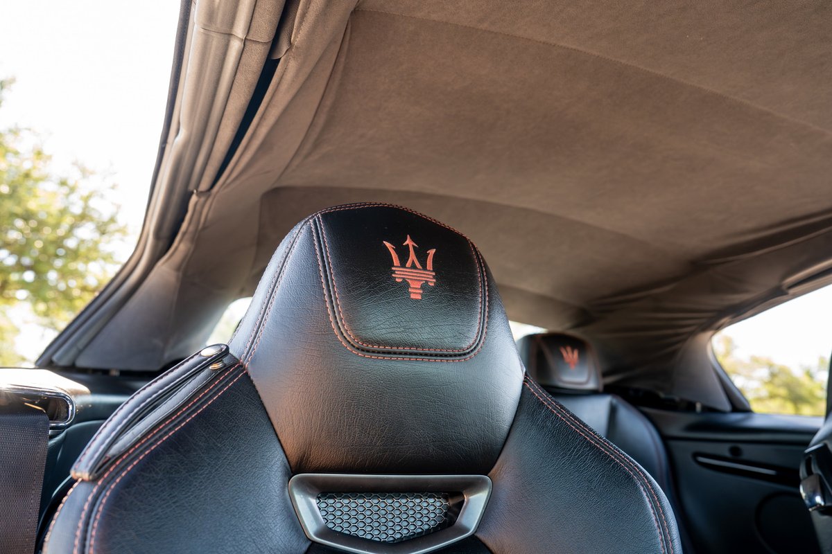 Black Maserati GranTurismo headrest with Trident logo and red stitching under a tan headliner.